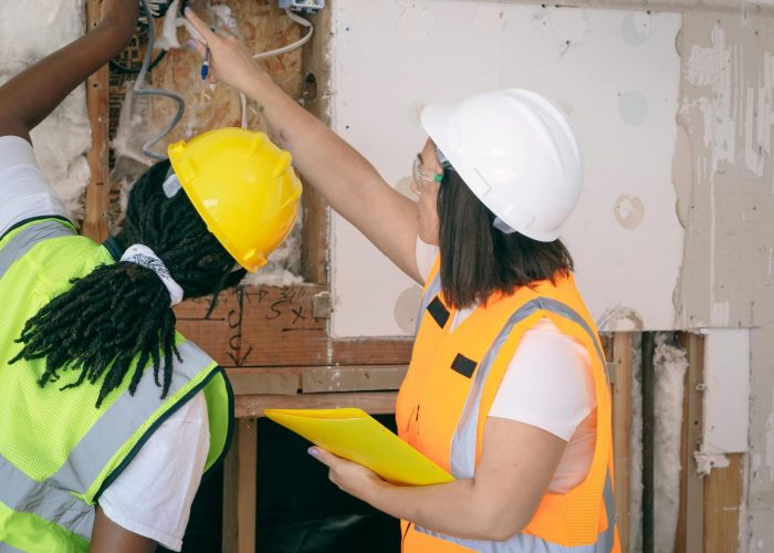 Two female engineers in safety gear inspecting wiring. Professional, safe, and collaborative workplace environment.